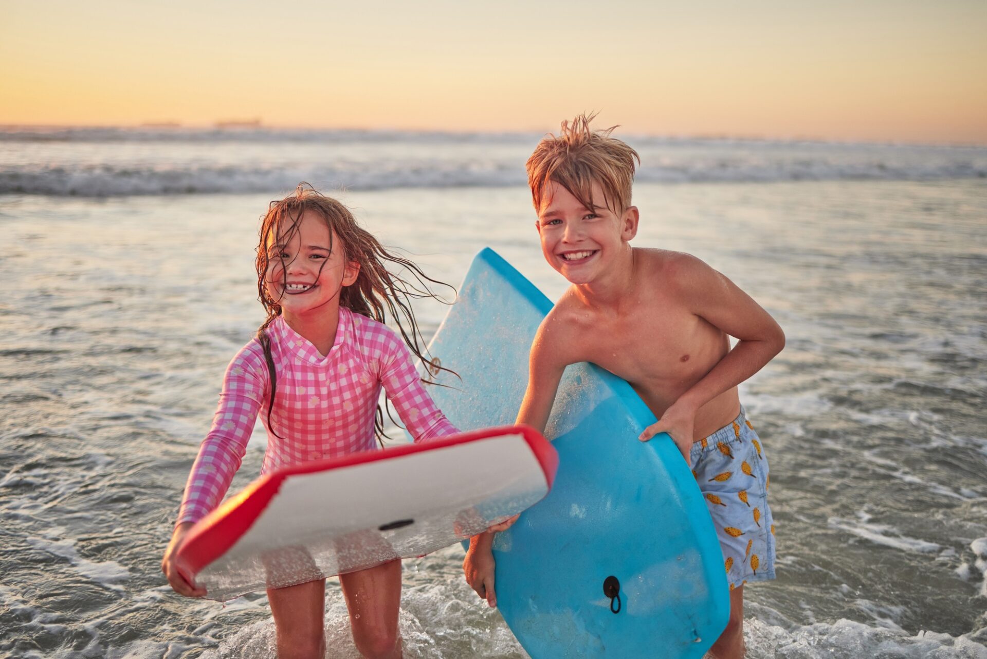 Zwei lachende Kinder surfen im Meer bei Sonnenuntergang während Bali Urlaub mit Familie