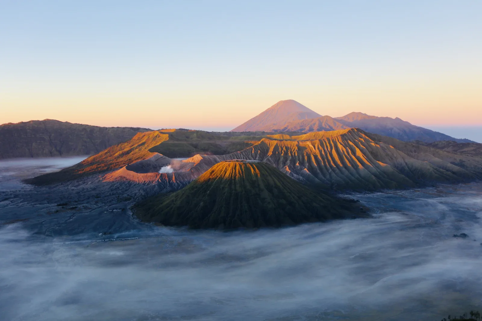Sonnenaufgang über dem Vulkan Mount Bromo in der Caldera, Java, Indonesien, mit Rauchfahnen und violettem Morgenlicht