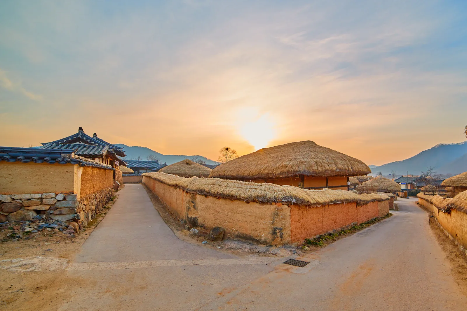 Traditionelles Dorf mit Megalithgrab und hohen Strohdachhäusern auf Sumba, Indonesien bei goldenem Licht